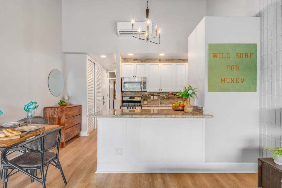 Cook and connect in a bright kitchen with white cabinetry, bar stools, and playful touches like the “Will Surf for Money” sign.
.
