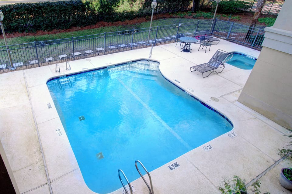 Community Pool and Lounge Chairs - Second pool angle with lounge chairs, pool deck, palms, and shaded seating nearby.