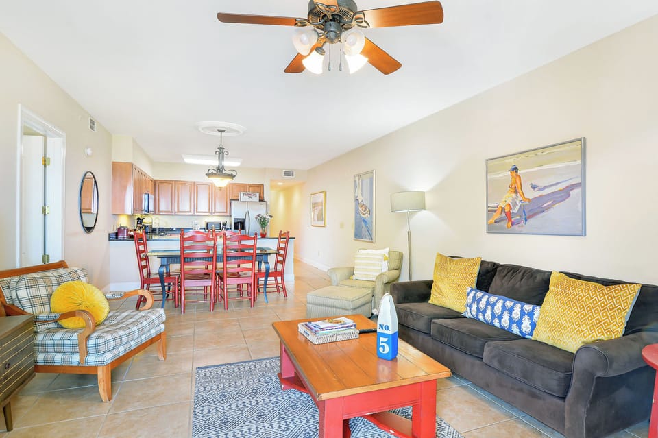 Living, Dining, and Kitchen Layout - Wide interior view shows sofa seating, dining table, kitchen, and bedroom hallway in one open layout.