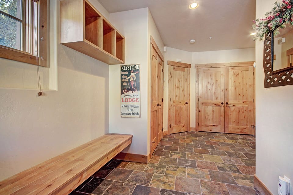 A foyer with wooden bench and shelving, slate tile floor, wooden doors, vintage Keystone Lodge ski poster on wall, window with natural light, and a small wall mirror by the entrance.