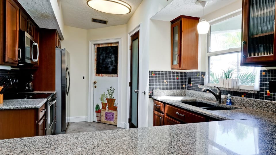 Granite countertops complement dark wood cabinets and black mosaic tile backsplash in the kitchen.