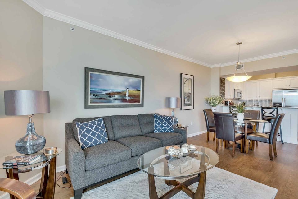 Living room with end tables, two side tables, two lamps looking towards dining table for 4