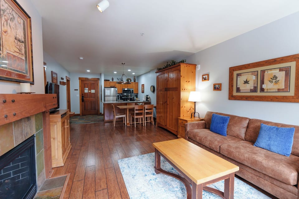 Relax in your spacious living area featuring warm wood accents, cozy fireplace, and comfortable seating that flows seamlessly into the fully-equipped kitchen.