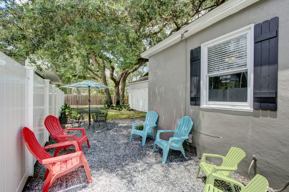Fenced Backyard Seating Area - Fully fenced backyard with gravel seating area, umbrella table, colorful chairs, and shaded space for dogs.
