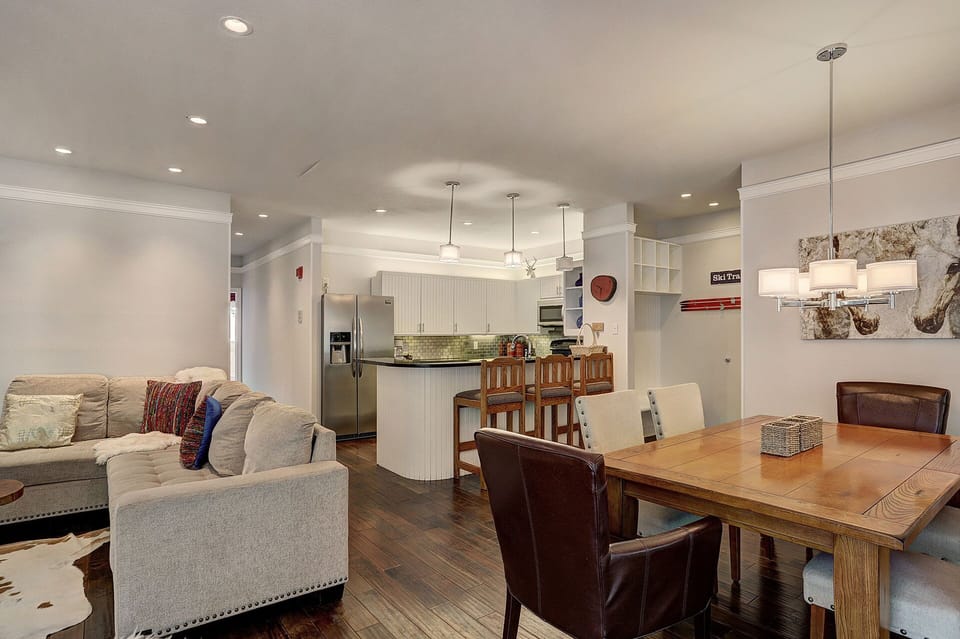 A modern open-concept living space with a kitchen, dining area, and living room. Features include a kitchen island with bar stools, a wooden dining table, and contemporary decor.