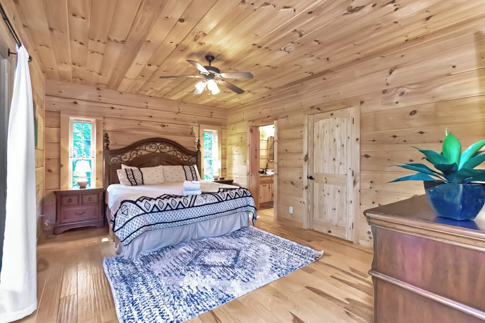 Wake up surrounded by warm knotty pine in the master bedroom at The Watchtower. A carved headboard and soft linens set a cozy mountain tone.