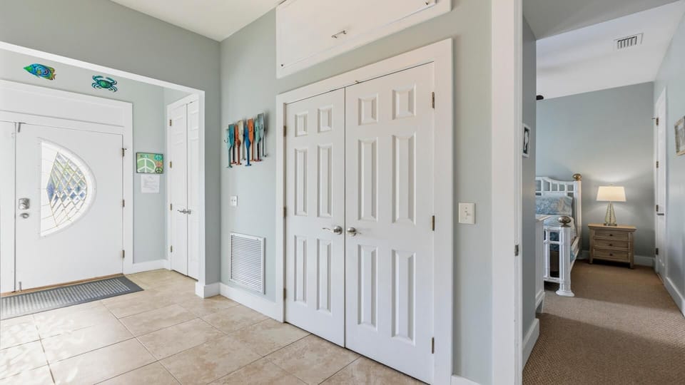 Entryway features beige tile flooring, a white front door with decorative glass, and pastel blue walls with coastal decor.