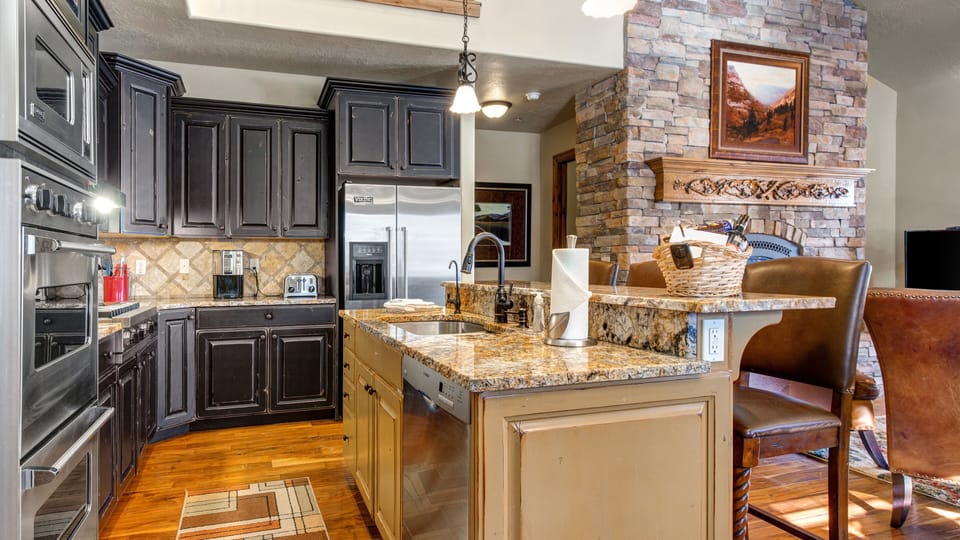 This chef's kitchen features premium stainless steel appliances, dark custom cabinetry, and granite countertops. The breakfast bar offers seating for quick meals in this elegant, mountain-modern space