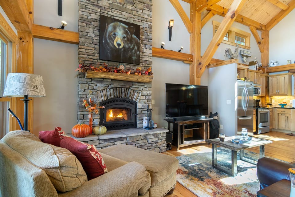 The open-concept living room boasts vaulted ceilings, a stone fireplace, and large windows that fill the space with natural light, creating a warm and inviting atmosphere.