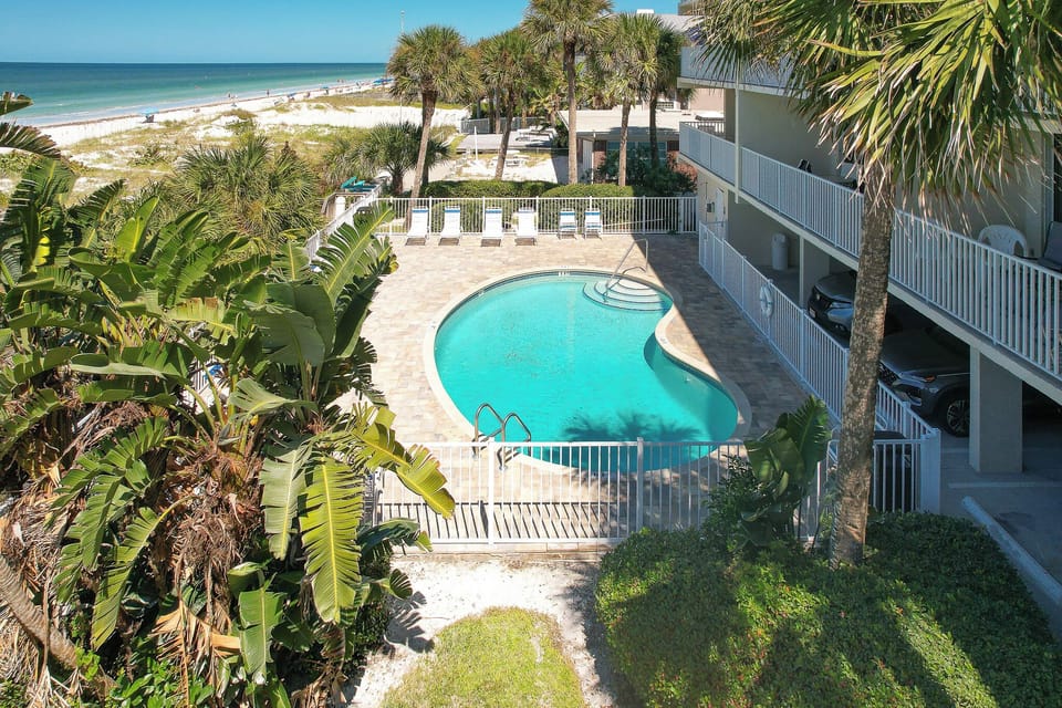 Beachfront property featuring a curved swimming pool surrounded by tropical palms and white sand beaches.