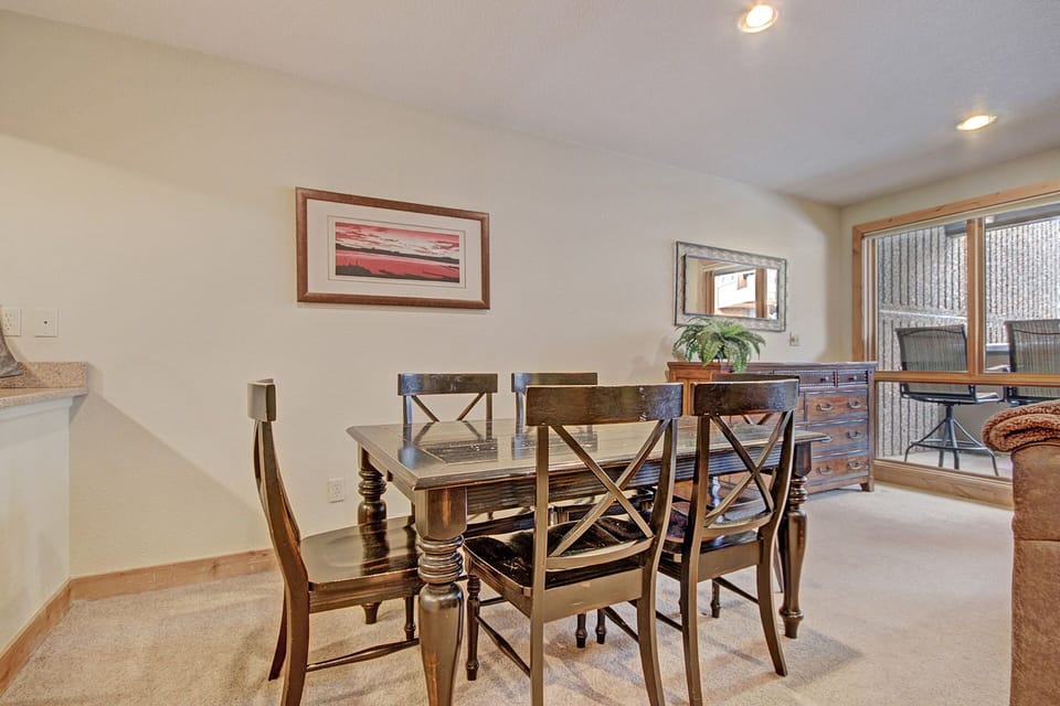 Dining area with a wooden table and chairs set, a framed picture on the wall, a dresser with a mirror above it, and a large window to the right letting in natural light.