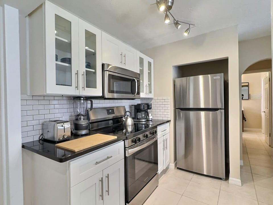 Fully equipped kitchen with stainless steel appliances, ample cabinetry, extended breakfast bar and stone-gray tile backsplash.
