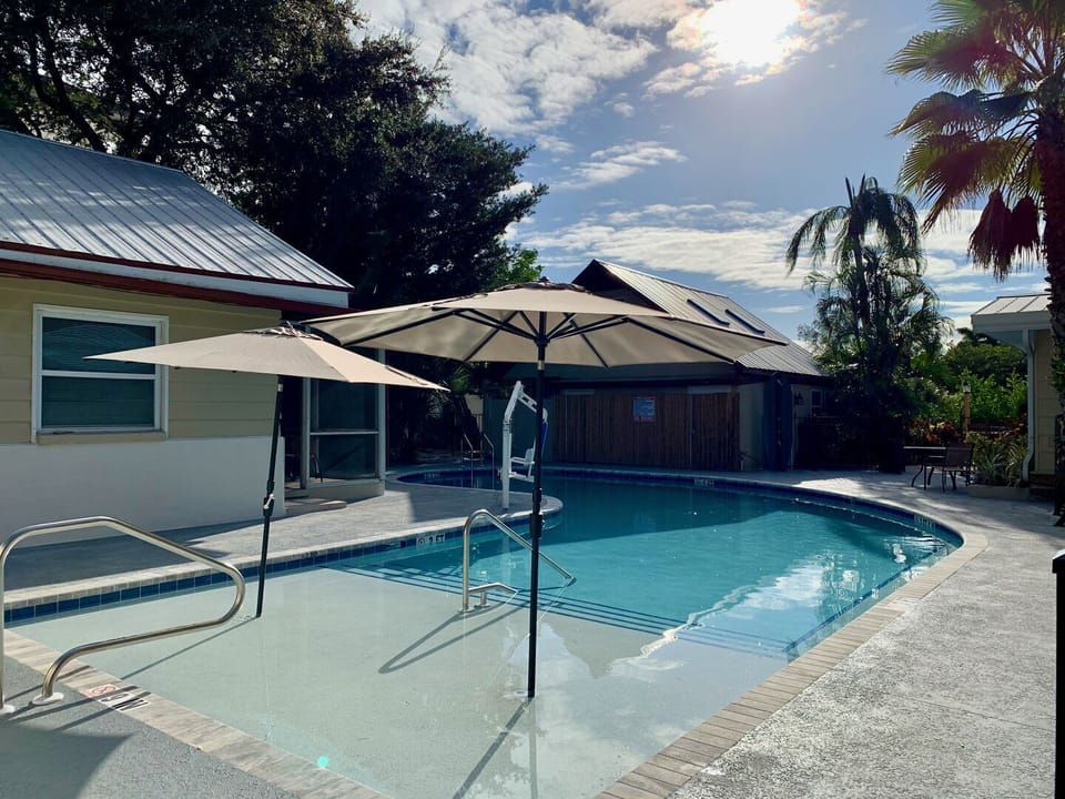 Community pool with umbrella table, chairs, and lush surrounding trees