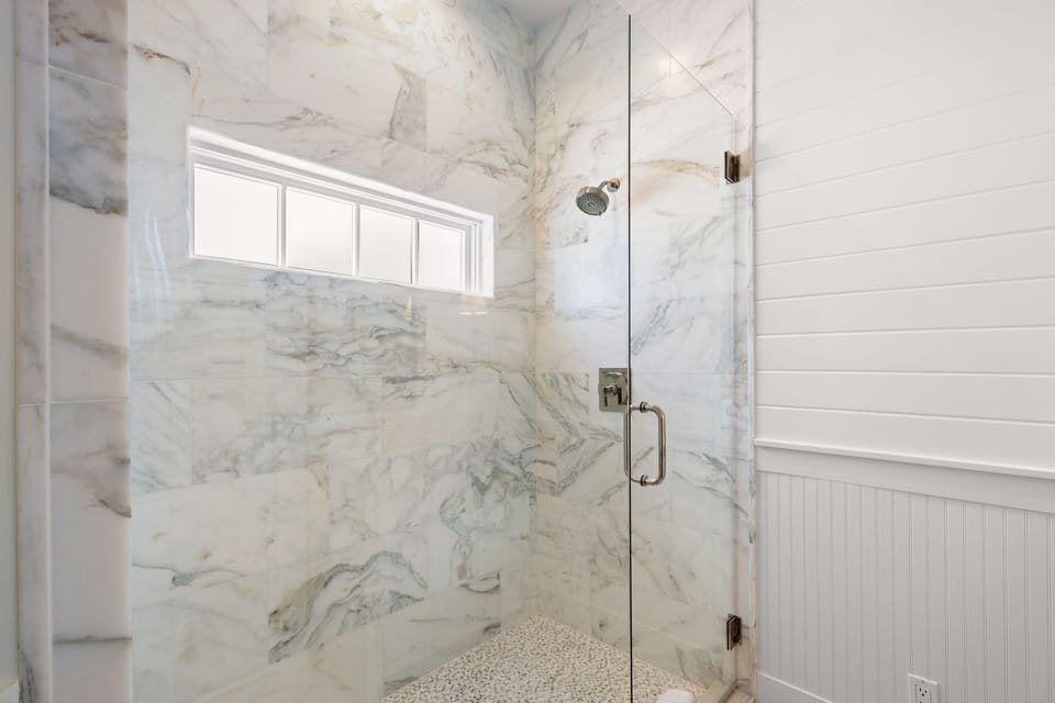 Marble walk-in shower brightened by a transom window
