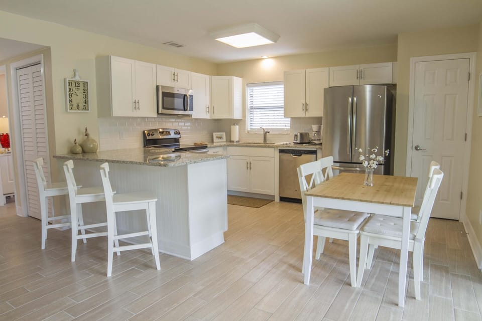 White cabinetry and granite countertops surround stainless steel appliances in the kitchen and dining area.