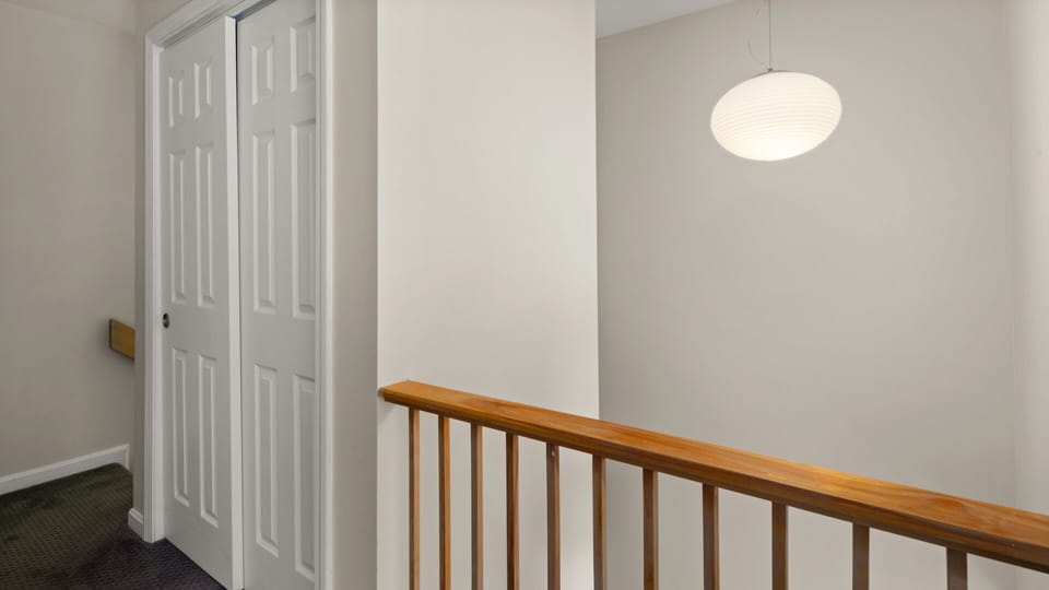 A hallway with beige walls, a hanging light fixture, wooden railing, and white sliding closet doors.