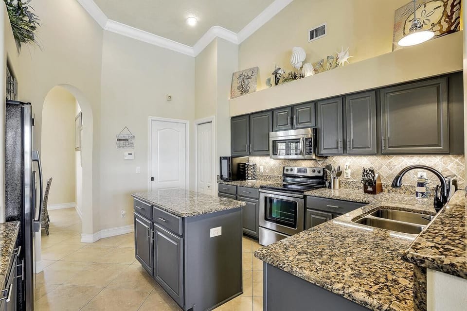 Under-cabinet lighting illuminates the granite backsplash and dark gray cabinetry in the open plan kitchen space.