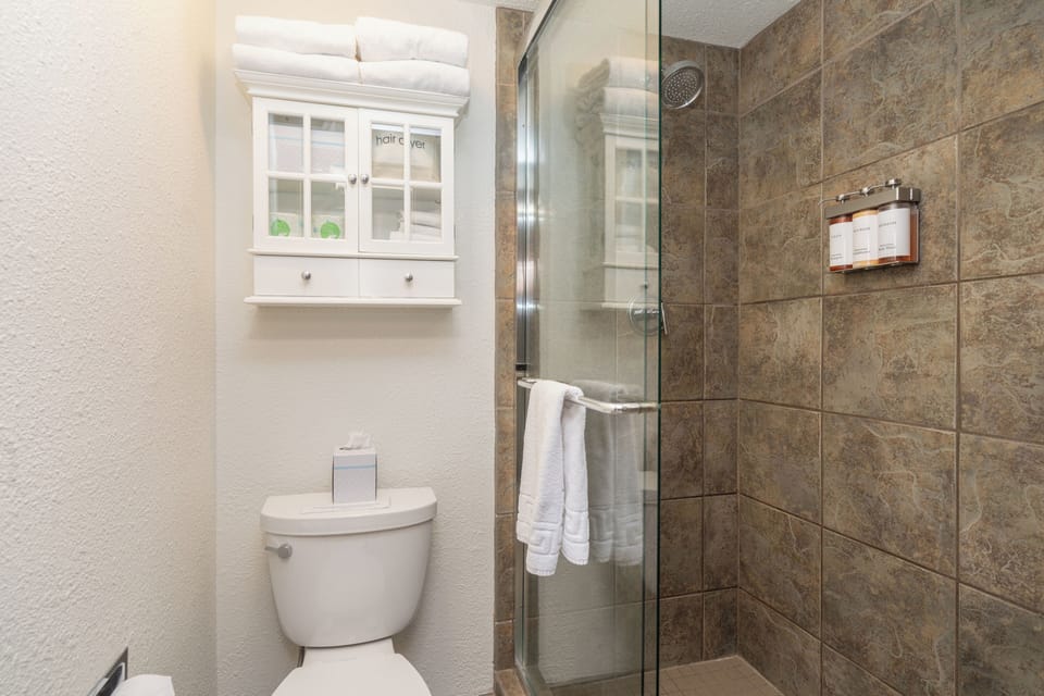 Your private bathroom features a sleek glass-enclosed shower with rustic stone tile, fluffy towels, and a charming cabinet for your essentials.