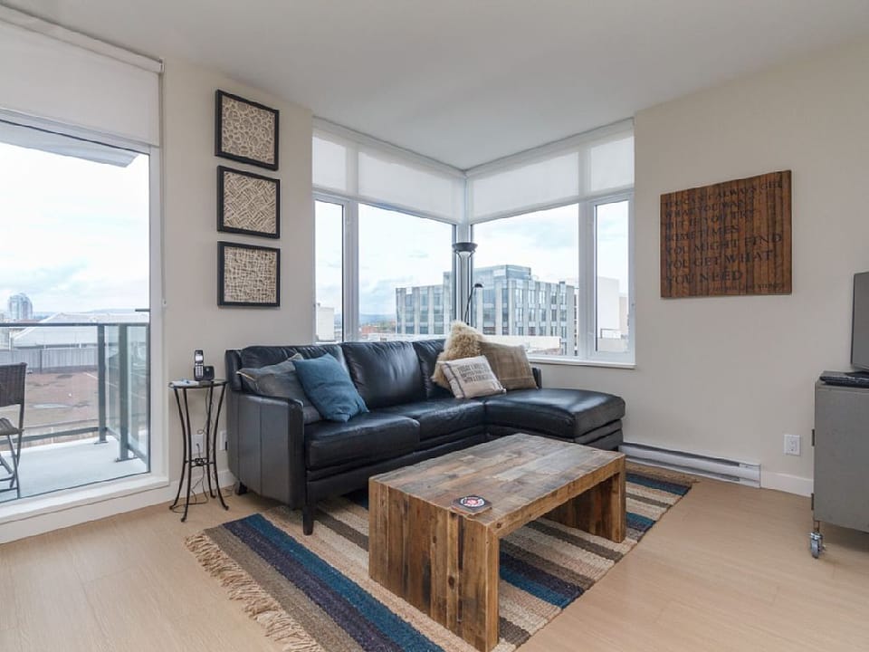 Floor-to-ceiling corner windows and city views—the perfect spot to kick back on the dark leather sofa by the rustic wooden coffee table.