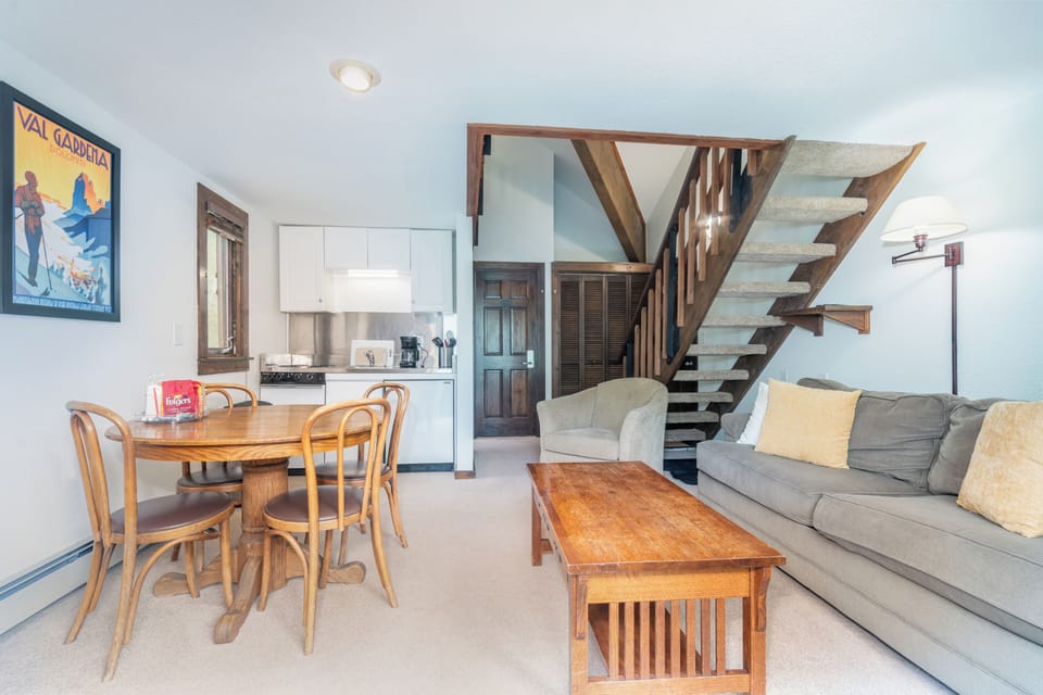 Your open-concept retreat blends comfort and style—cozy seating, a warm dining nook, a full kitchen ready for home-cooked meals, and stunning wooden stairs leading to more space above.