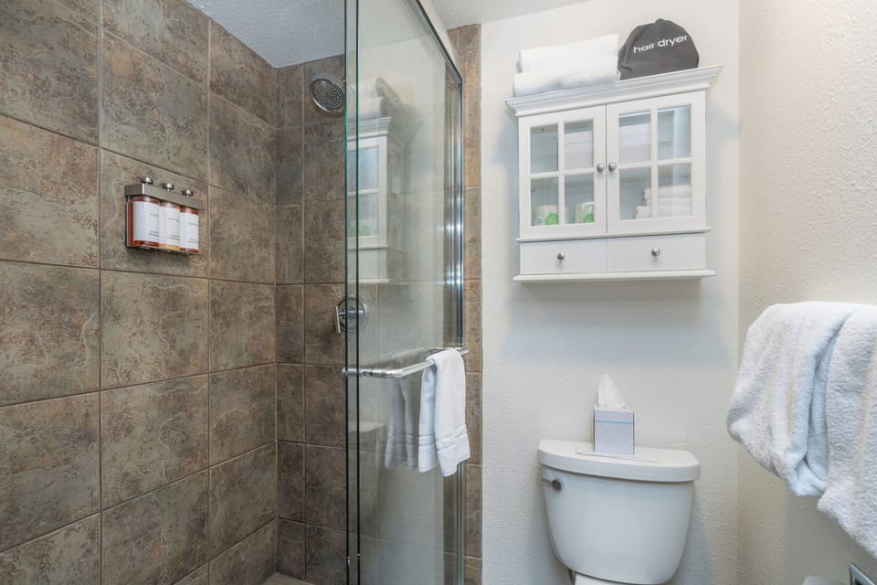 Step into your private bathroom with a modern glass-enclosed shower, fresh towels, and thoughtful amenities waiting for you. Everything's been arranged for your comfort.