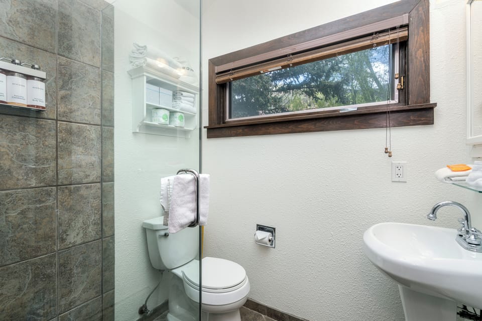 Step into your private bathroom with a tiled walk-in shower, modern fixtures, and natural light streaming through the window overlooking peaceful greenery.