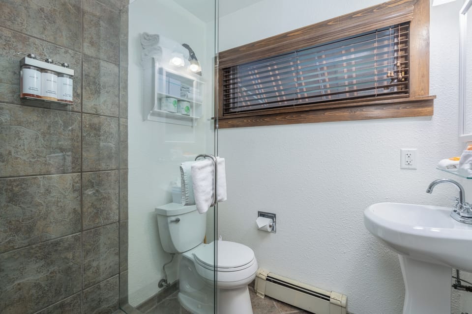 Your private bathroom features a walk-in shower with elegant stone tile, a pedestal sink, and crisp white linens—a refreshing space to start and end your day.