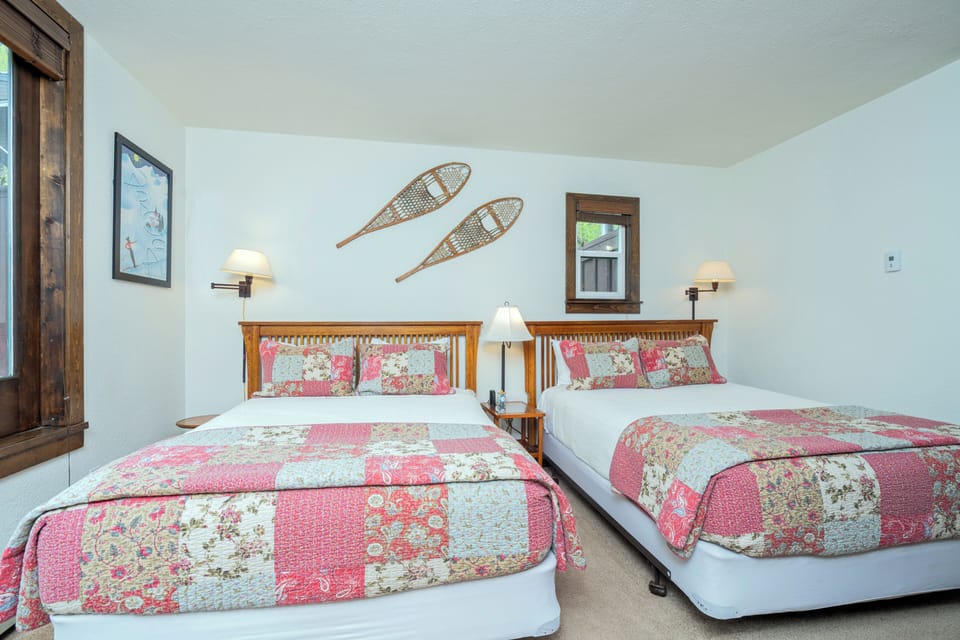 Relax in your cozy bedroom with two plush beds dressed in charming patchwork quilts. Warm sconces and rustic snowshoe décor create a welcoming mountain retreat vibe.