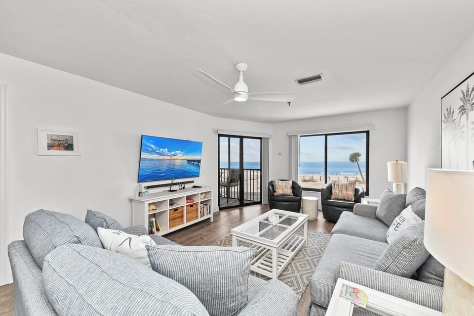 Step into your coastal haven where plush gray seating faces stunning ocean views through floor-to-ceiling windows.