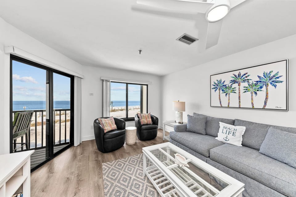 Sink into the plush gray sofa and soak up stunning ocean views through floor-to-ceiling windows in this bright, coastal-themed living room.