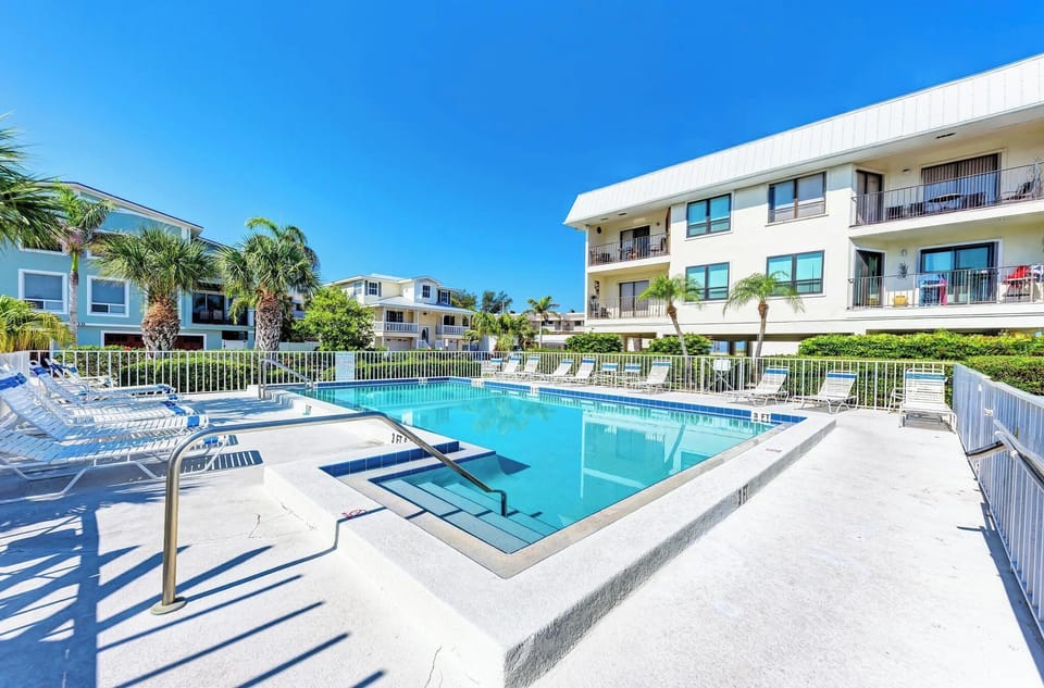 Sparkling pool area surrounded by tropical landscaping and modern buildings under endless blue skies.