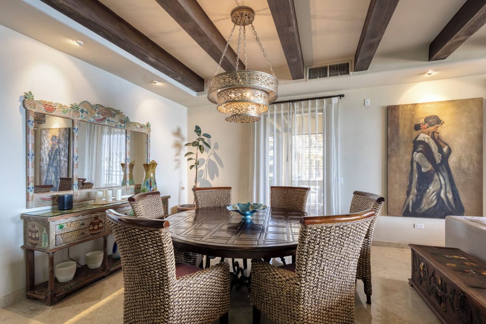 Step into an elegant dining space where rustic ceiling beams meet artful design. Gather around the handcrafted table beneath a stunning chandelier, surrounded by unique décor and natural light streaming through sheer curtains.
