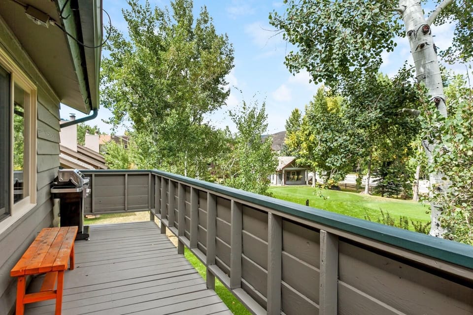 Roomy deck with gas grill and bench seating opens to beautiful green space.