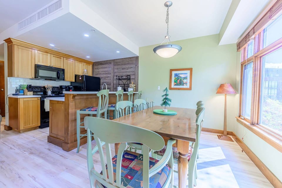 Open-concept kitchen and dining area with full-size table, breakfast bar, and large windows for natural light.