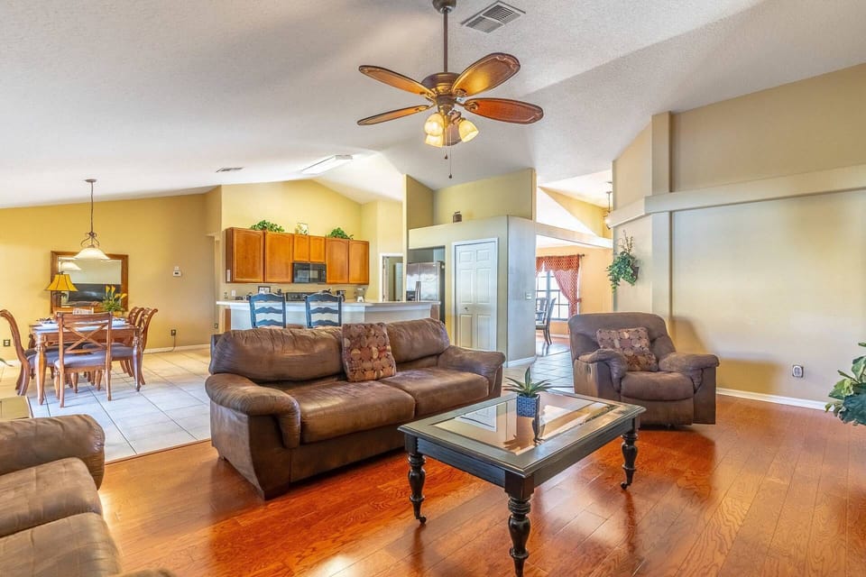 Living room with hardwood floors, tall ceilings and reclining seating that opens to the kitchen and second dining area.