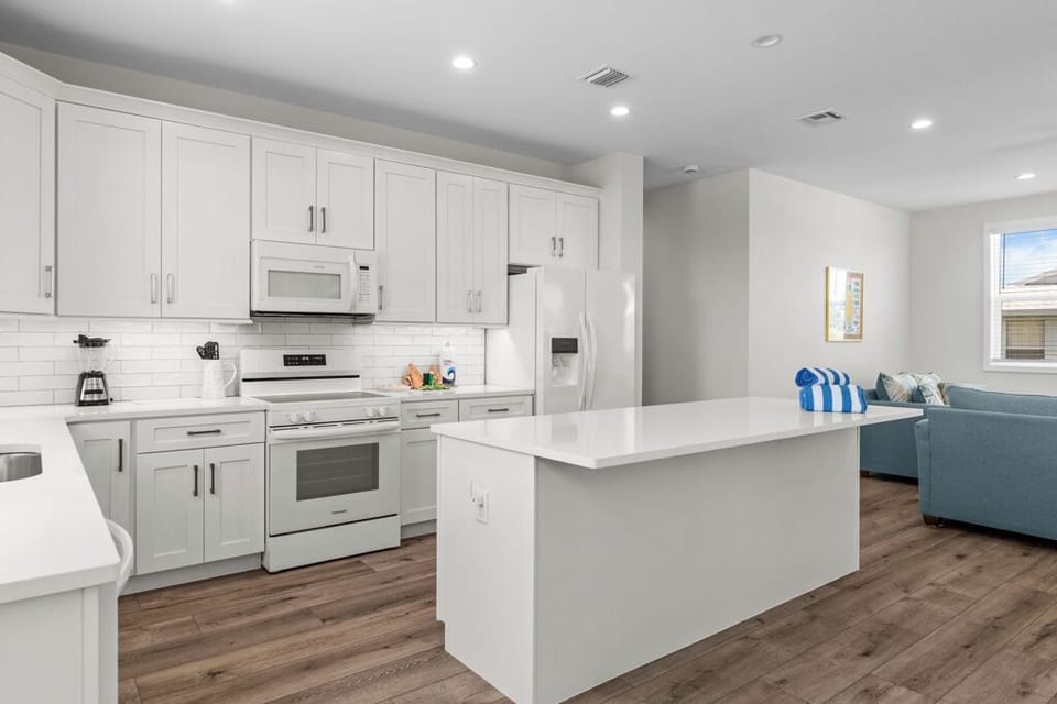 Sleek and inviting kitchen with all-white appliances, shaker-style cabinets, quartz countertops, and a large island—ideal for casual meals or entertaining in style.