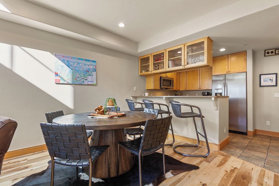 Your dining area features a warm wood table surrounded by stylish woven chairs, perfectly positioned near your fully equipped kitchen for memorable meals.