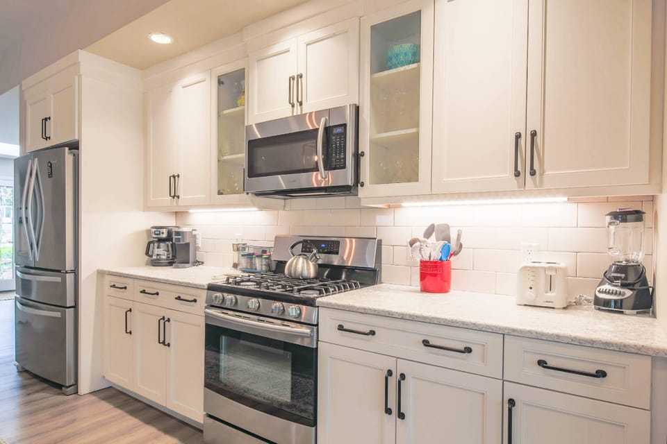 This gorgeous kitchen features white cabinetry, tiled backsplash, undercabinet lighting and stainless steel appliances.