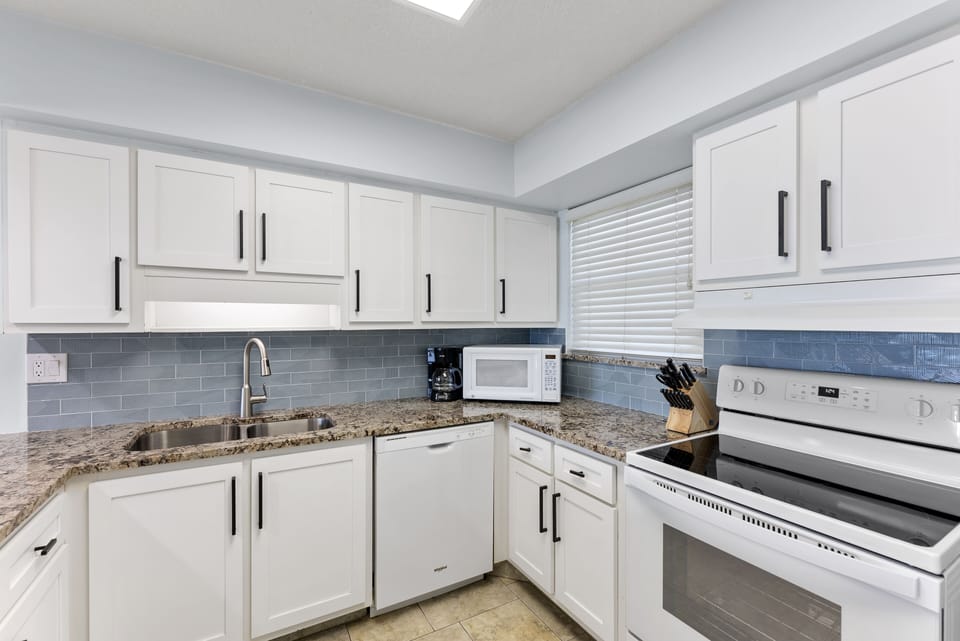 Fully equipped kitchen with white cabinetry, modern appliances, and a stylish backsplash.