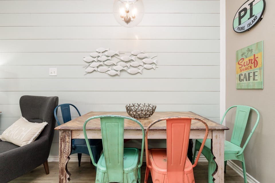 Your coastal-inspired dining space features colorful chairs and beach-themed décor, perfect for enjoying meals together.