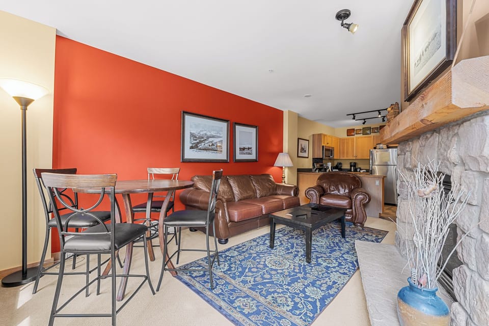 Unwind in your cozy living space featuring rich leather seating, a stone fireplace, and an open kitchen perfect for mountain getaway meals.
