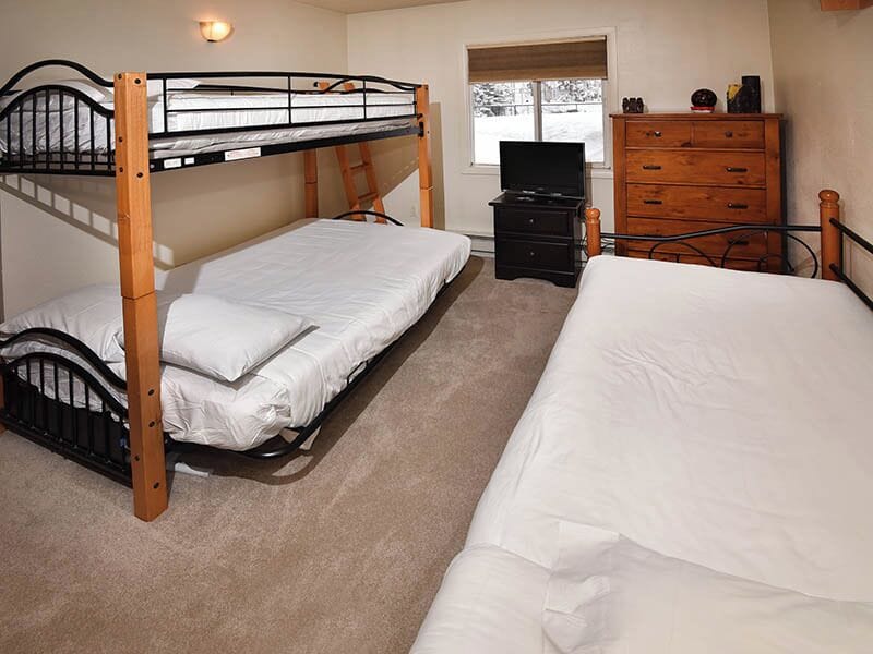Your group-friendly bedroom sleeps everyone comfortably with a bunk bed and full bed, all dressed in crisp white linens. Natural light streams in while warm wood furniture adds a cozy, welcoming touch.