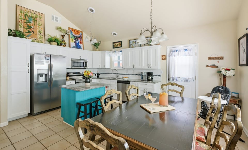Kitchen & dining — turquoise island, white cabinets, dark wood table with cocktails & 'Gone Fishing' sign