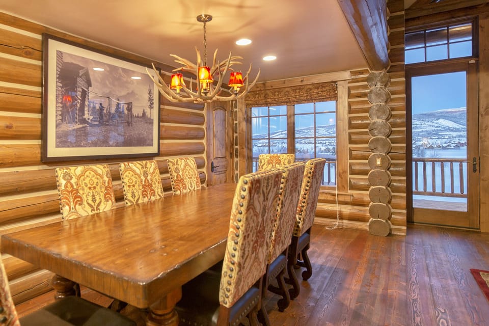 Gather around this stunning rustic dining room where warm log walls and an antler chandelier create the perfect mountain retreat atmosphere. You'll love sharing meals here while gazing at breathtaking snowy vistas through large windows.