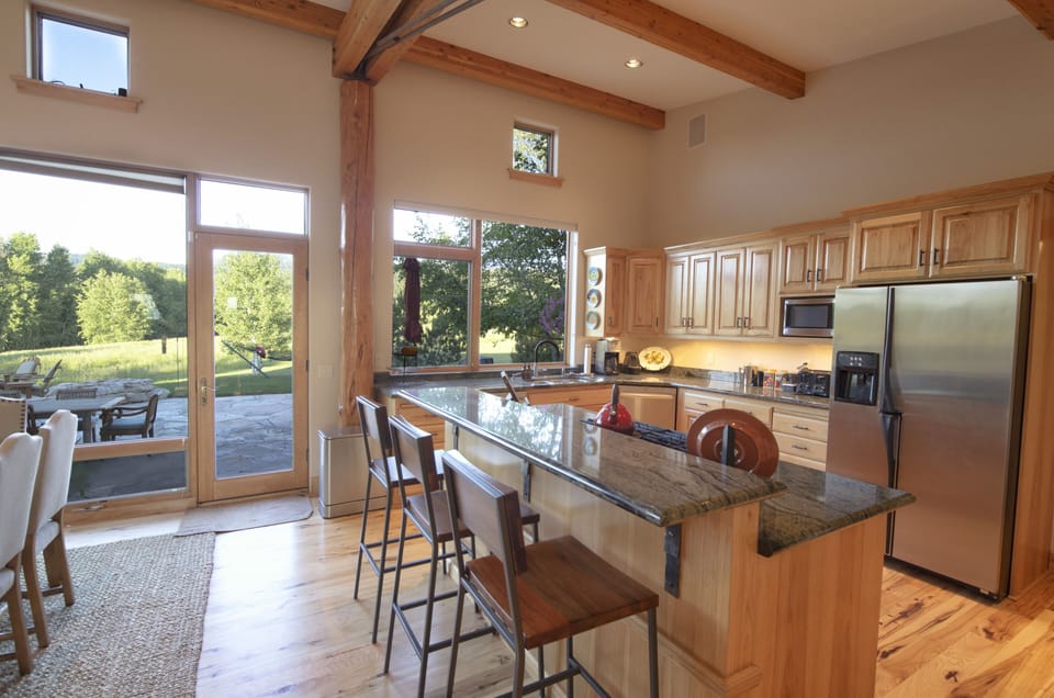 Your dream kitchen awaits with soaring beamed ceilings and granite countertops where you'll gather around the island for morning coffee while sunlight streams through expansive windows.