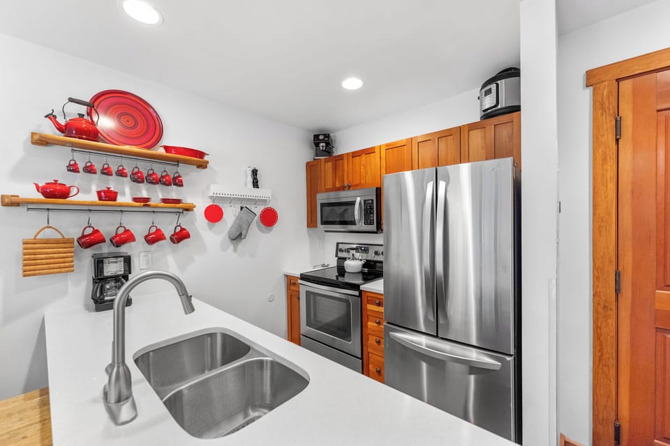 Your fully equipped kitchen features warm wood cabinetry, stainless steel appliances, and charming red cookware for memorable home-cooked meals.