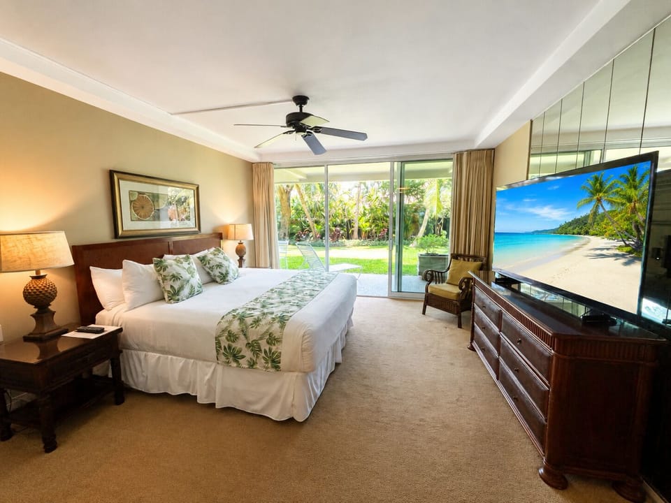 Your serene bedroom overlooks a lush tropical garden through floor-to-ceiling glass doors, inviting natural light and a direct connection to the outdoors. Sink into the plush king bed after a day of exploration and unwind completely.