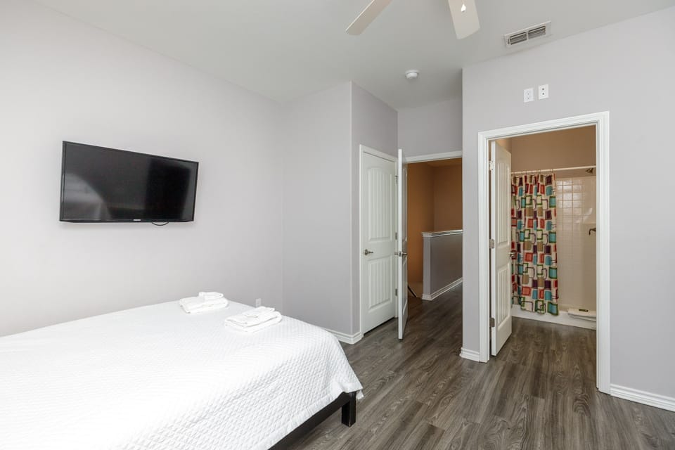 Your contemporary bedroom features crisp linens, a wall-mounted TV for entertainment, and your own private bathroom with colorful shower tile accents.