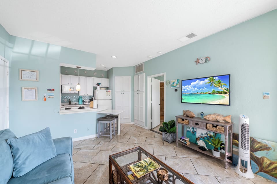 Relax in your bright coastal living space with soothing mint walls, tropical decor, and ocean views on the large TV.