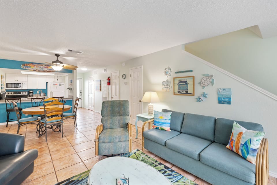 Relax in your bright open living space featuring comfortable coastal-themed furniture and a fully equipped kitchen perfect for family gatherings.